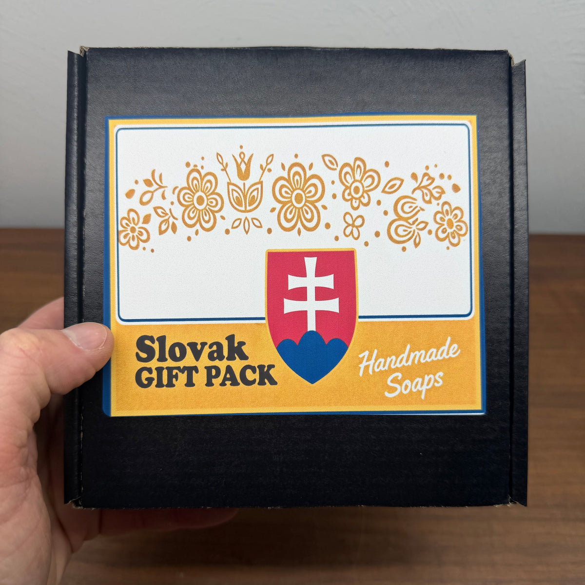 Handmade soap packaging with Slovak design elements held by a hand.