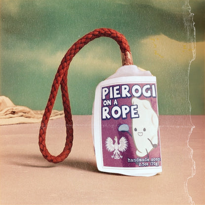 Handmade soap on a rope with a red rope labeled 'Pierogi on a Rope' on a textured surface.